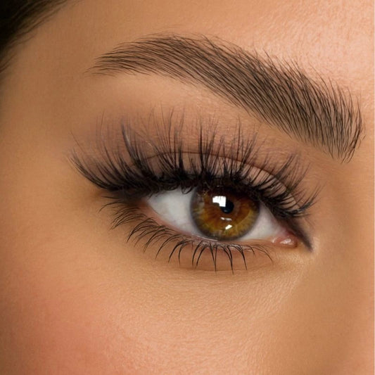 Close-up of a woman's eye wearing voluminous, fluffy false eyelashes with natural brown eye color and perfectly groomed eyebrows.